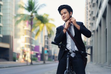 Takım elbiseli Asyalı işadamı işe gitmek için sabah işe giderken yolda bisiklet sürmek için güvenlik kaskı takıyor. Çevre Taşımacılığı