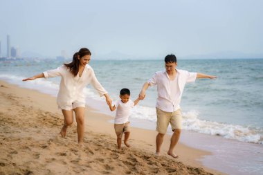 Babası, annesi ve oğlu olan Asyalı bir aile yazın Tayland 'da tatildeyken sahilde koşuyor.