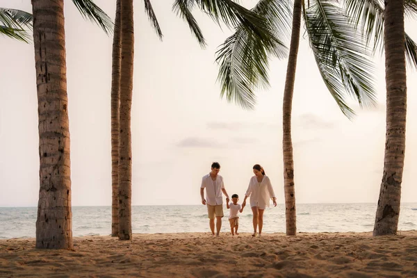 息子を持つアジアの家族は タイの夏の休暇中にヤシの木とビーチ沿いを歩いています — ストック写真