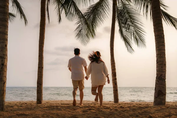 アジアのカップルは タイの夏の休暇中にヤシの木とビーチビーチの海で走って手をつないでいます — ストック写真