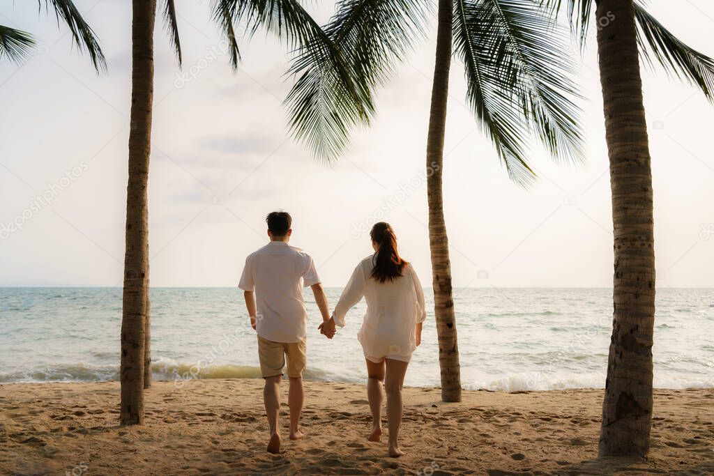 Asian couple is running and holding hands on a beachfront beach sea with coconut trees while on vacation in the summer in Thailand.