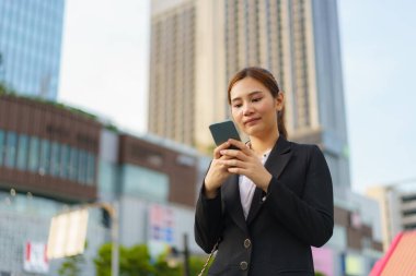Bangkok, Tayland 'da ofis binalarının arka planında cep telefonu kullanan Asyalı yönetici kadın.