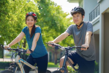 Kask takan Asyalı çift, hem fiziksel hem de zihinsel sağlık için mahallesinde bisiklet turuna hazırlanıyor..