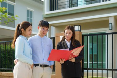 Asyalı emlakçı kadın dosyasında ev detaylarını genç Asyalı çift aşığına gösteriyor ve satın almak istiyor. Yeni bir ev alıyorum.