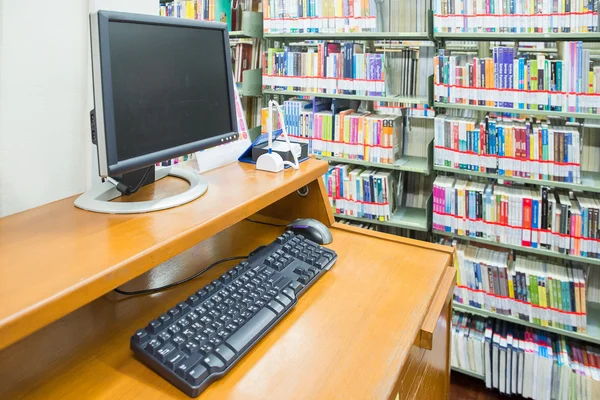 Комп'ютер у бібліотеці з безліччю книг і полиць на задньому плані — стокове фото