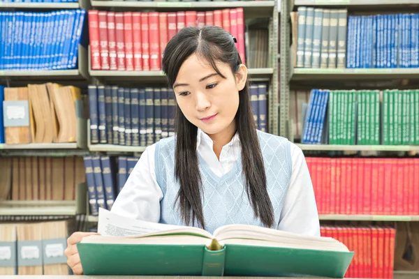 Asiatiska student med öppen bok läsa den i college library — Stockfoto