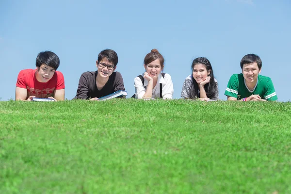 Grupo de estudiantes al aire libre tumbados en el suelo y sonriendo —  Fotos de Stock