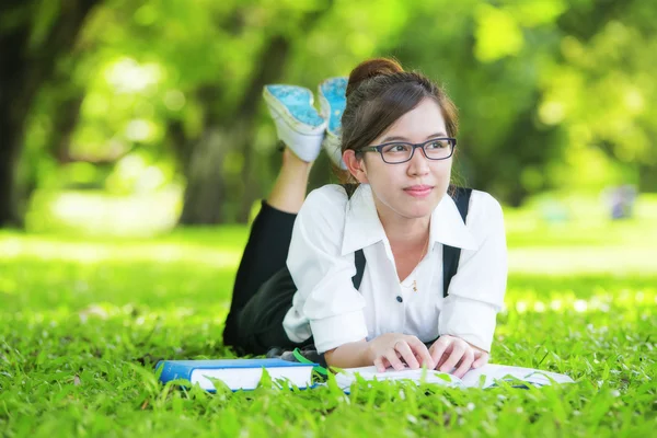 Sorridente studente casuale sdraiato sul libro di lettura erba — Foto Stock