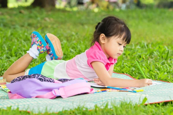 Chica joven al aire libre acostado en la hierba y el dibujo — Foto de Stock