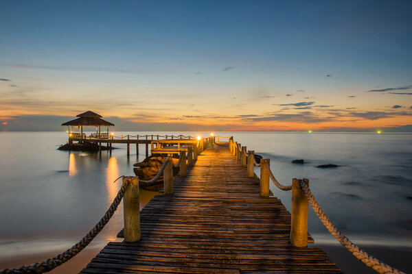 Пейзаж пирса деревянного моста между закатом
