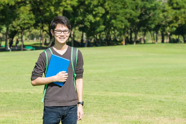 Estudante asiático segurando livros e sorrindo enquanto estava no parque um — Fotografia de Stock