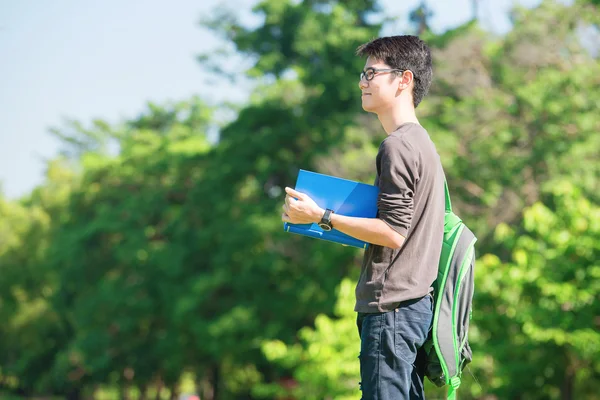 Asiatique étudiant tenant des livres et souriant tout en se tenant dans le parc un — Photo