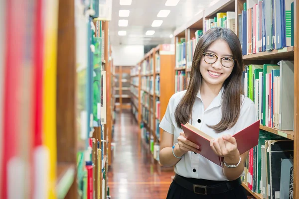 Estudante asiático em leitura uniforme na biblioteca da universidade — Fotografia de Stock