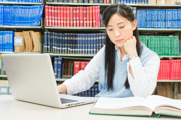 Estudante asiático usando computador portátil na biblioteca da faculdade — Fotografia de Stock