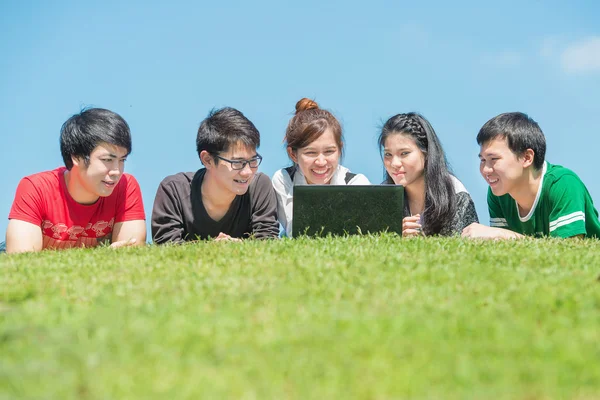 Groupe de jeunes étudiants utilisant un ordinateur portable ensemble dans le parc — Photo