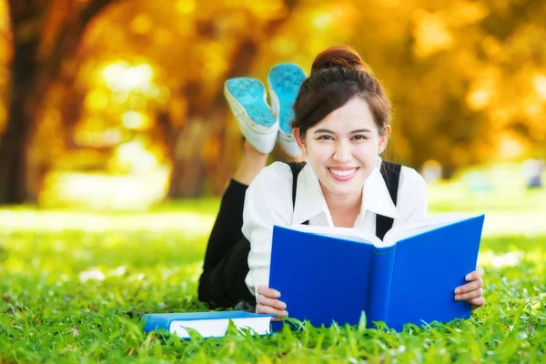 Sorridente studente casuale sdraiato sul libro di lettura erba — Foto Stock