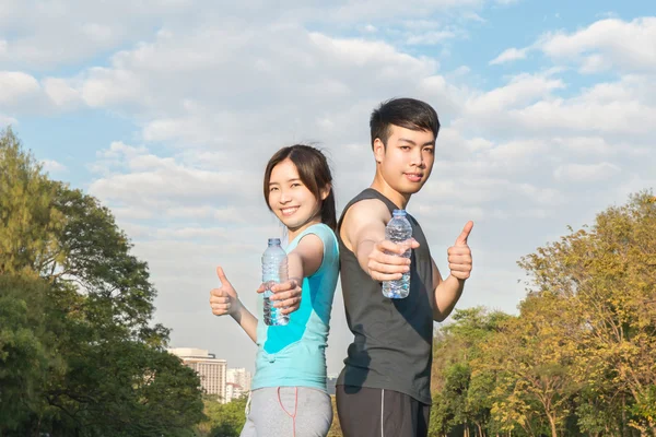 Jovem asiático homem e mulher bebendo água de uma garrafa e polegar — Fotografia de Stock