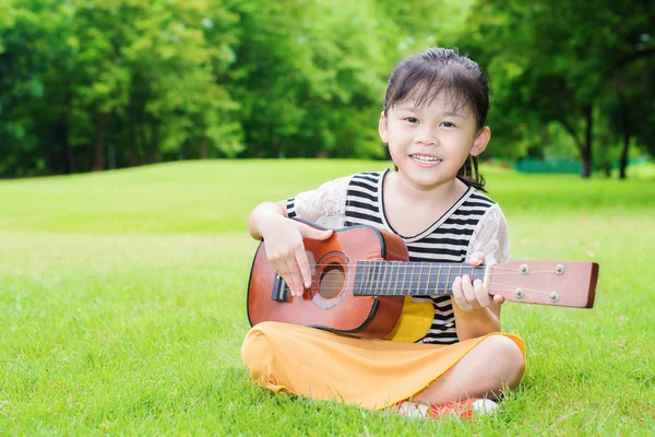 Asiática niña sentada en la hierba y jugar ukelele en parque — Foto de Stock