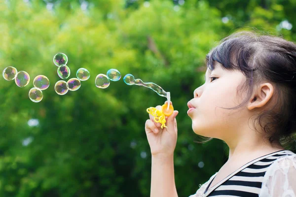 Asian little girl blowing soap bubbles in green park — Stock Photo, Image