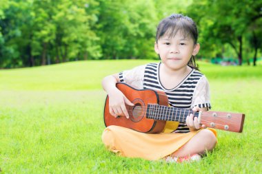 Asyalı çocuklara ot ve oyun ukulele parkta oturan
