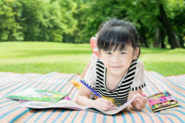 Asian girl kids outdoors lying on the grass and drawing