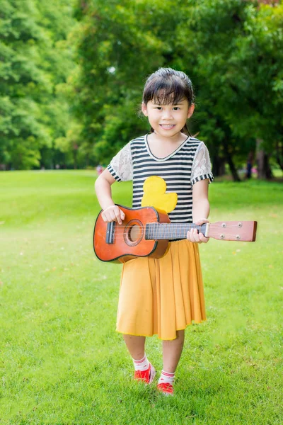 Asiático niños sentado en la hierba y jugar ukelele en parque — Foto de Stock