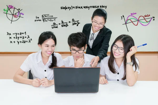 Professor asiático assistindo estudante usando laptop na mesa na sala de aula — Fotografia de Stock