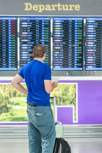 Joven con mochila en el aeropuerto cerca del horario de vuelo —  Fotos de Stock