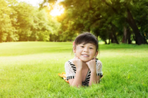 Маленькая азиатская девочка лежит на зеленой траве — стоковое фото