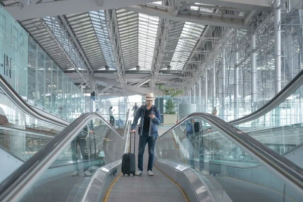 Jonge Aziatische man met bagage naar beneden de roltrap in luchthaven. — Stockfoto