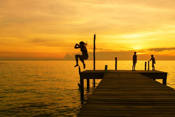 Silhuetas de mulher saltam no mar do cais — Fotografia de Stock