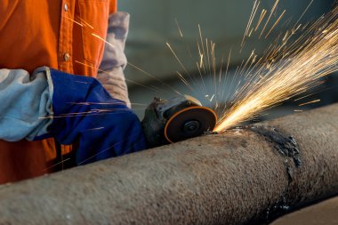 Öğütücüyle metal kesen bir işçi. Demir öğütürken kıvılcımlar