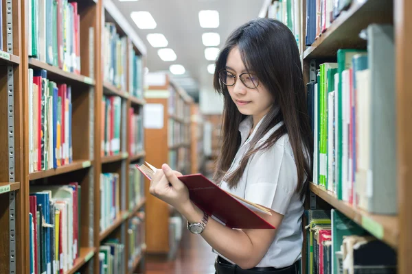 Estudante asiático em leitura uniforme na biblioteca da universidade — Fotografia de Stock