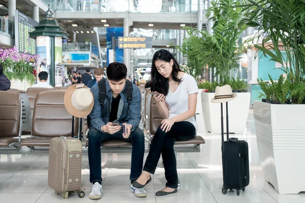 젊은 아시아 부부는 airpor에 앉아있는 동안 스마트 휴대 전화를 사용 하 여 — 스톡 사진