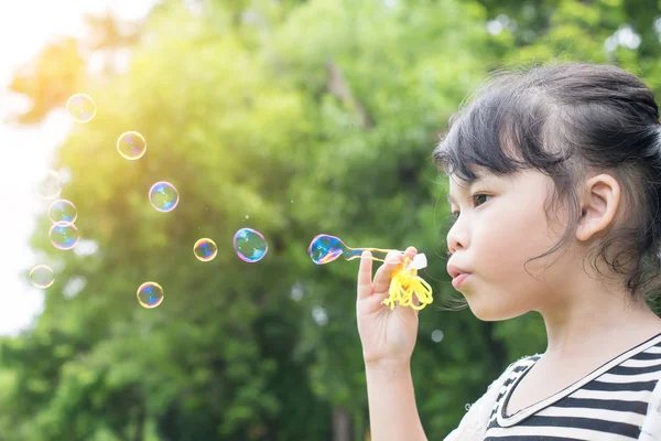 Asian little girl blowing soap bubbles in green park — Stock Photo, Image
