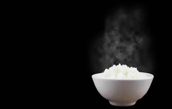 Aislado de arroz caliente al vapor en un tazón blanco con vapor blanco sobre fondo oscuro Imagen de archivo