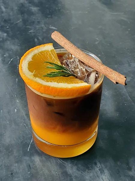 Top view of a ice coffee garnish with orange, rosemary and cinnamon on stone background.