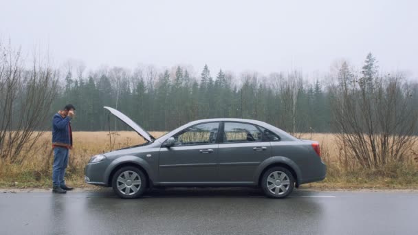 Man en trasig bil och öppnar huven i skogen. Bilen gick plötsligt sönder på en landsväg ner under körning. — Stockvideo