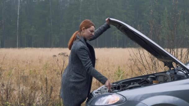 Vista laterale. Donna d'affari aprire cofano auto e guardando il motore. Autista donna in piedi accanto al veicolo rotto vicino alla foresta. Concetto incidente stradale. — Video Stock