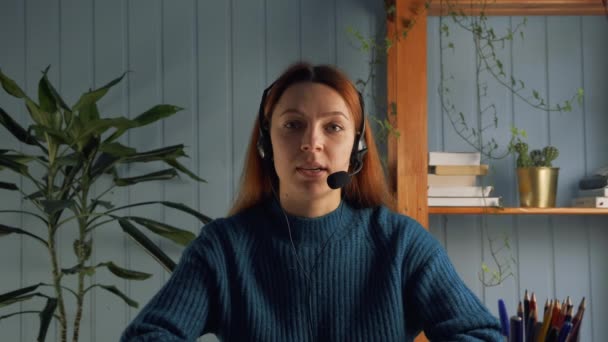 Kopfschussfrau mit Kopfhörer sitzt drinnen und winkt Abonnenten, die das Video aufnehmen. Vorstellungsgespräch per Videocall-App, moderne Laptop-Nutzung, Streaming-Kommunikationsteilnehmer — Stockvideo