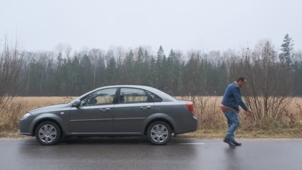 Un conductor masculino coloca una señal de parada de emergencia en la carretera. Coche con luces de parada de emergencia encendidas. — Vídeos de Stock