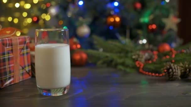 Mulher coloca biscoitos de gengibre em uma mesa de madeira com leite. Decorações de Natal, árvore de Natal, guirlanda bokeh no fundo. — Vídeo de Stock