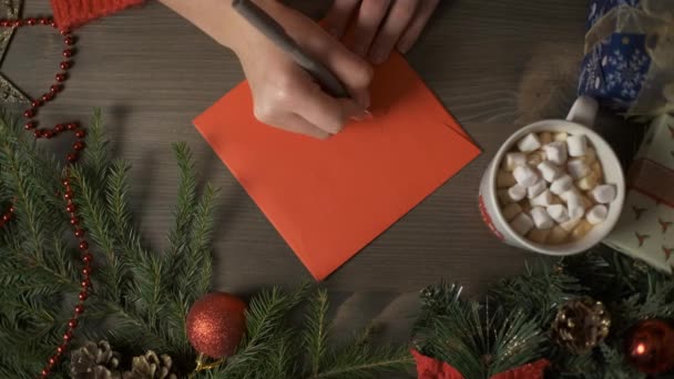 Eine Frau schreibt mit einem Stift eine Weihnachtskarte, umgeben von Weihnachtsdekoration. — Stockvideo