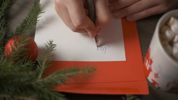 Eine Frau schreibt mit einem Stift eine Weihnachtskarte, umgeben von Weihnachtsdekoration. — Stockvideo