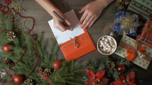 Eine Frau schreibt mit einem Stift eine Weihnachtskarte, umgeben von Weihnachtsdekoration. — Stockvideo