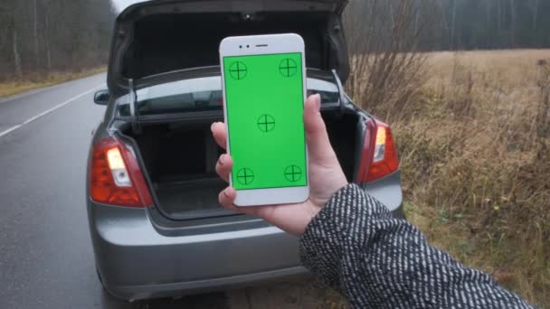 Close up hand of woman using vertically smartphone blank screen and blur of his broken car parked in woods. Contacting car technician or need help concept — Stock Video