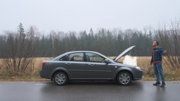 Jeune homme faisant du stop sur une route avec sa voiture en panne — Video