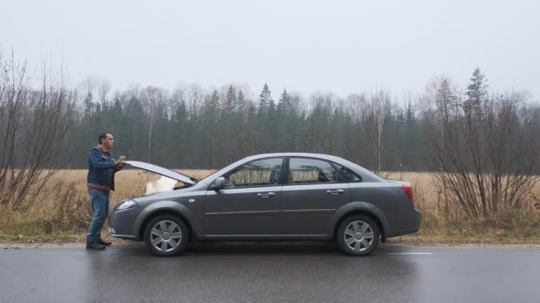 En ung man en trasig bil och öppnar motorhuven. Bilen gick plötsligt sönder på en landsväg. — Stockvideo