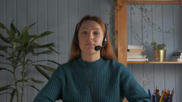 Mujer joven con auriculares con micrófono manteniendo una conversación en línea, estudiando a distancia o discutiendo proyectos con colegas. — Vídeos de Stock