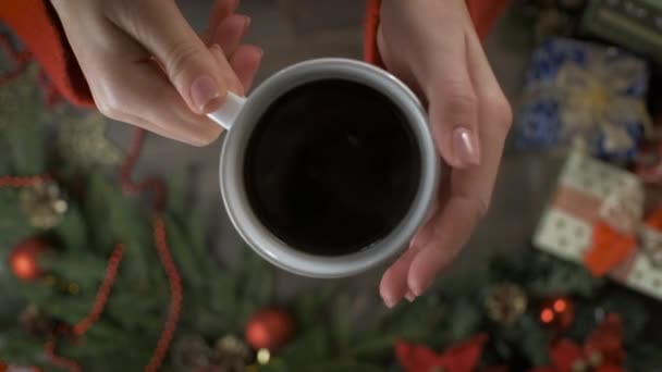 Hot coffe in female hands. Unrecognizable girl holding warm cozy coffe on background table decorated with Christmas decorations. — Vídeos de Stock